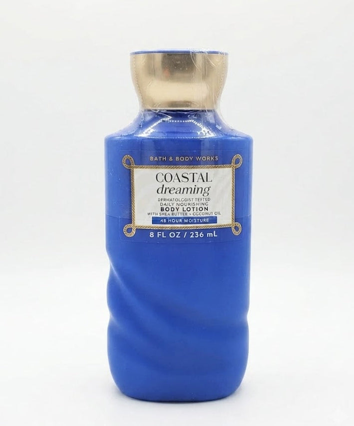 A detailed close-up of the rear bottle of Bath & Body Works Coastal Dreaming lotion, which is in sharp focus, with the other two bottles of the trio in the foreground slightly blurred.